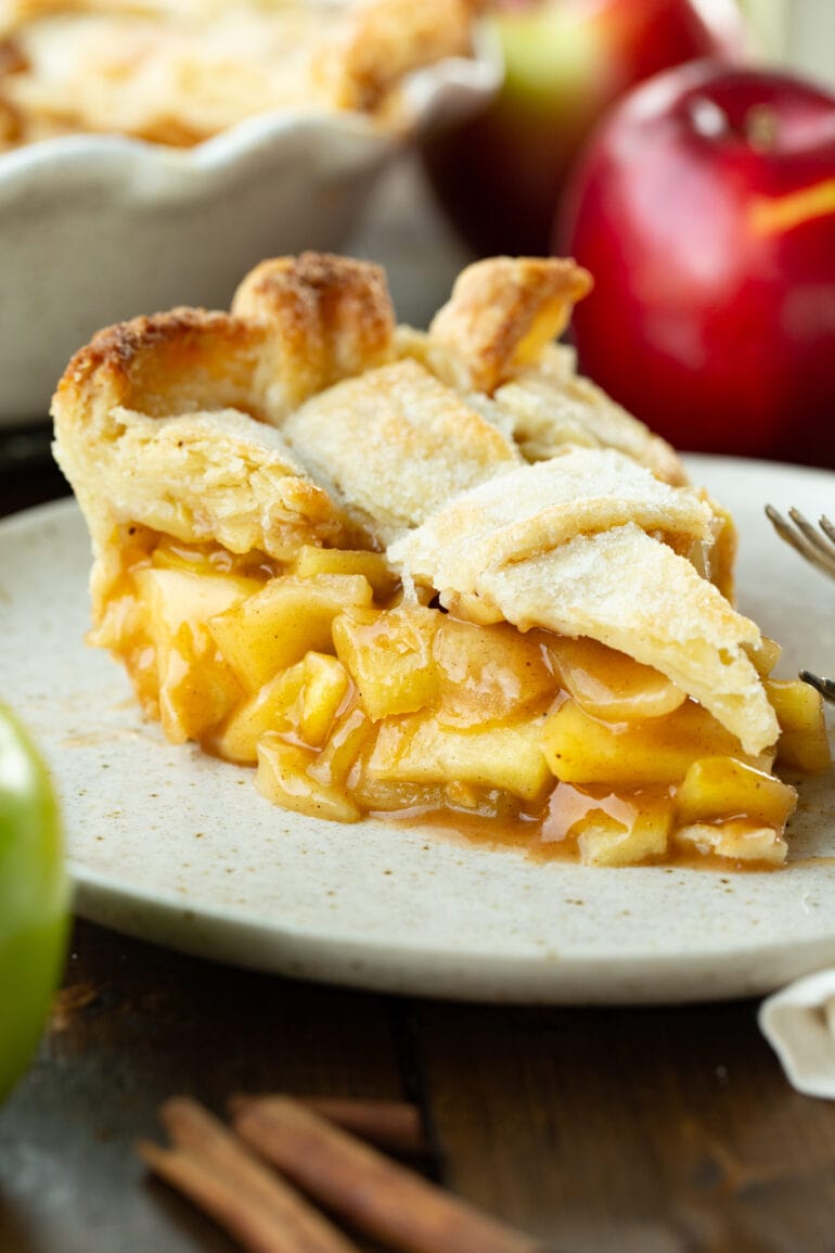 a photo of a slice of homemade apple pie sitting on a small dessert plate. The crust is golden and a lattice top and the filling is gooey with cinnamon and perfectly soft apples.