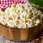A wooden bowl on a red and white checkered napkin full of creamy macaroni salad.