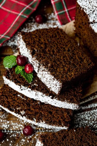 a photo of several slices of moist gingerbread loaf laying on each other topped with whole cranberries and greenery