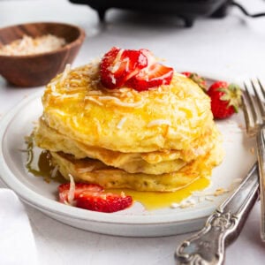 a stack of golden pancakes dripping with syrup and topped with sliced strawberries