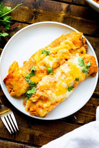 a photo of two bean and cheese enchiladas smothered in melty cheese on a white dinner plate