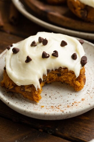 a photo of thick pumpkin chocolate chip cookie topped with cream cheese frosting and sprinkled with mini chocolate chips
