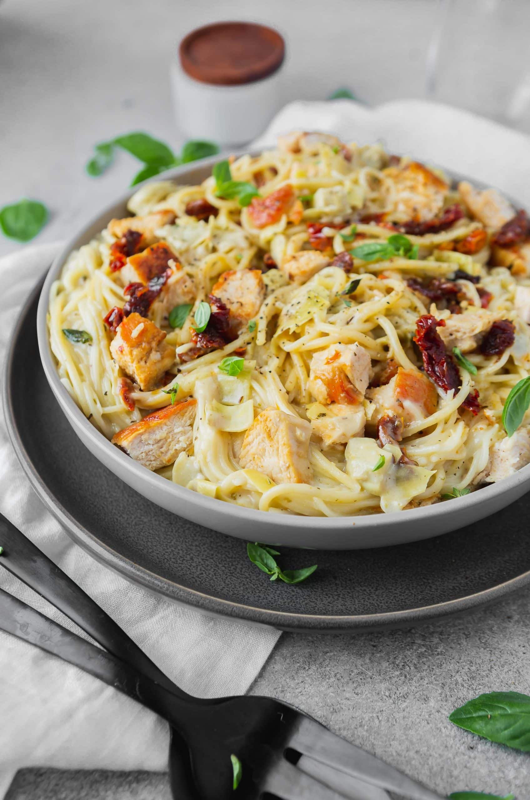 a photo of creamy chicken pasta with sun dried tomatoes and fresh basil on top.