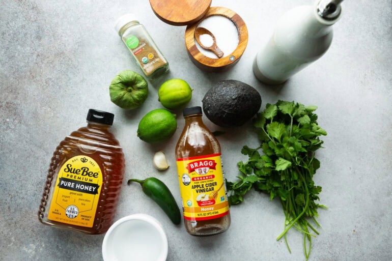 all the ingredients for cilantro lime dressing including cilantro, avocado, limes, apple cider vinegar, honey, jalapeno, tomatillo, and seasonings