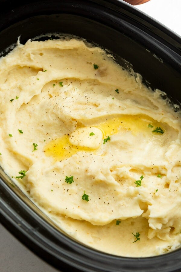 Creamy crockpot mashed potatoes topped with melted butter and fresh herbs