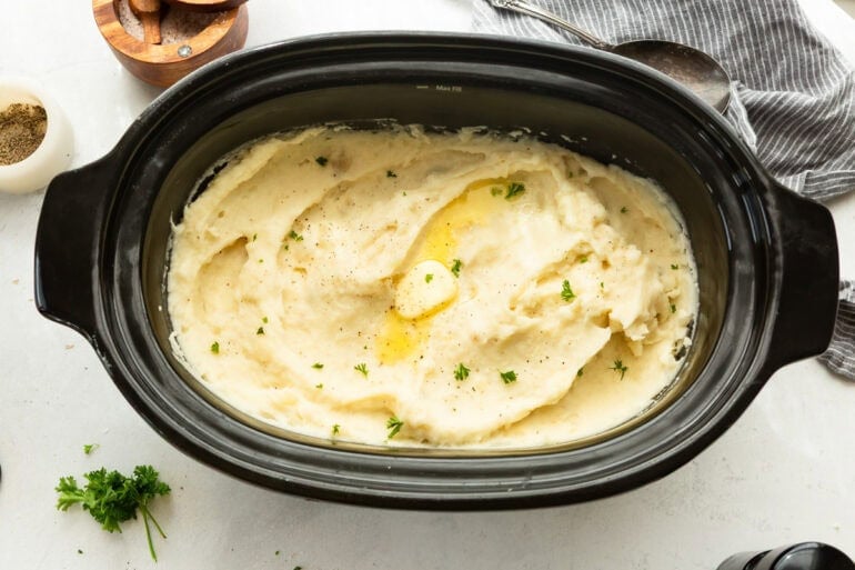 a large crockpot full of creamy mashed potatoes topped with a pat of melting butter