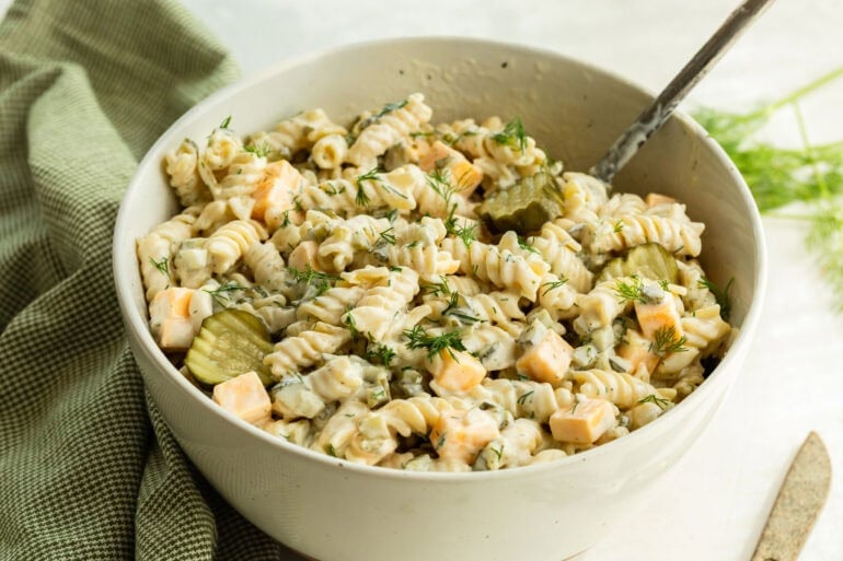 A large bowl of dill pickle pasta salad with noodles in a creamy sauce, pickles, and cheddar cheese