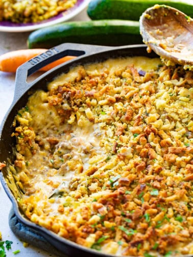 a photo of a creamy zucchini sausage casserole with stuffing on top in a cast iron skillet with a scoop taken out