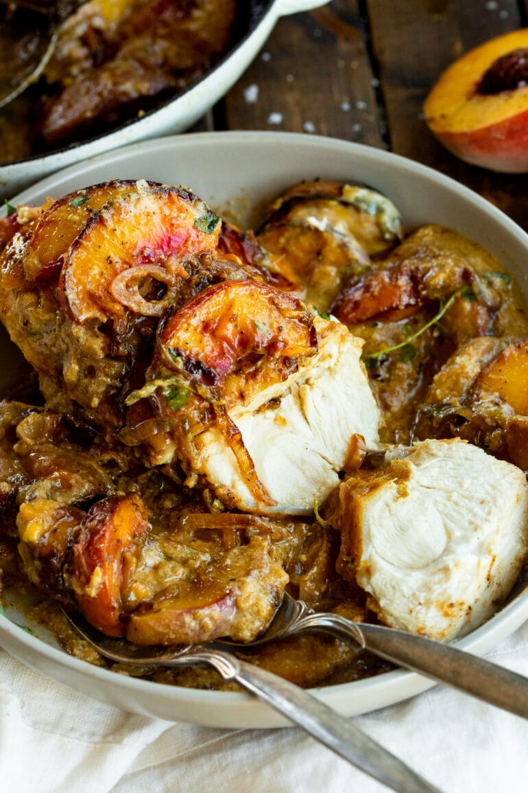 a photo of a serving dish full of creamy peach chicken breasts with one sliced open to see the juicy center