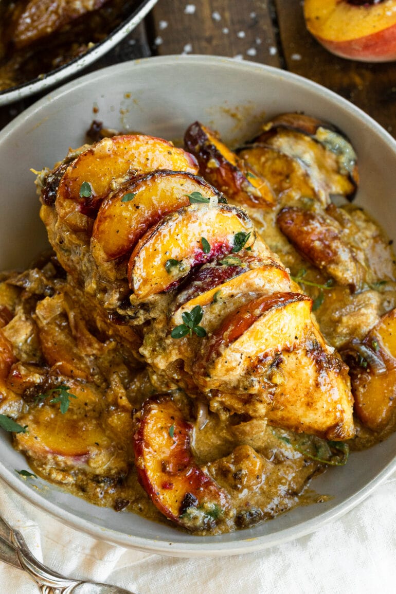 a photo of a serving dish full of baked chicken breasts topped with a creamy sauce and sliced baked peaches