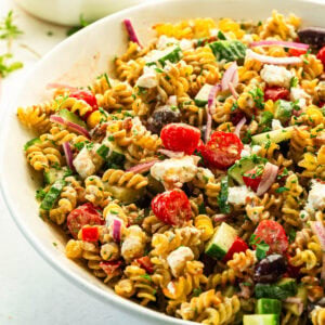 a large white serving bowl of crispy Greek pasta salad with feta, kalamata olives, tomatoes and a creamy dressing