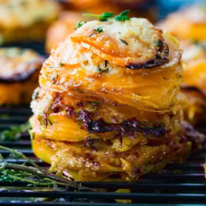 A photo of a stack of thinly sliced sweet potatoes layered with gruyere and parmesan cheese and topped with fresh thyme.