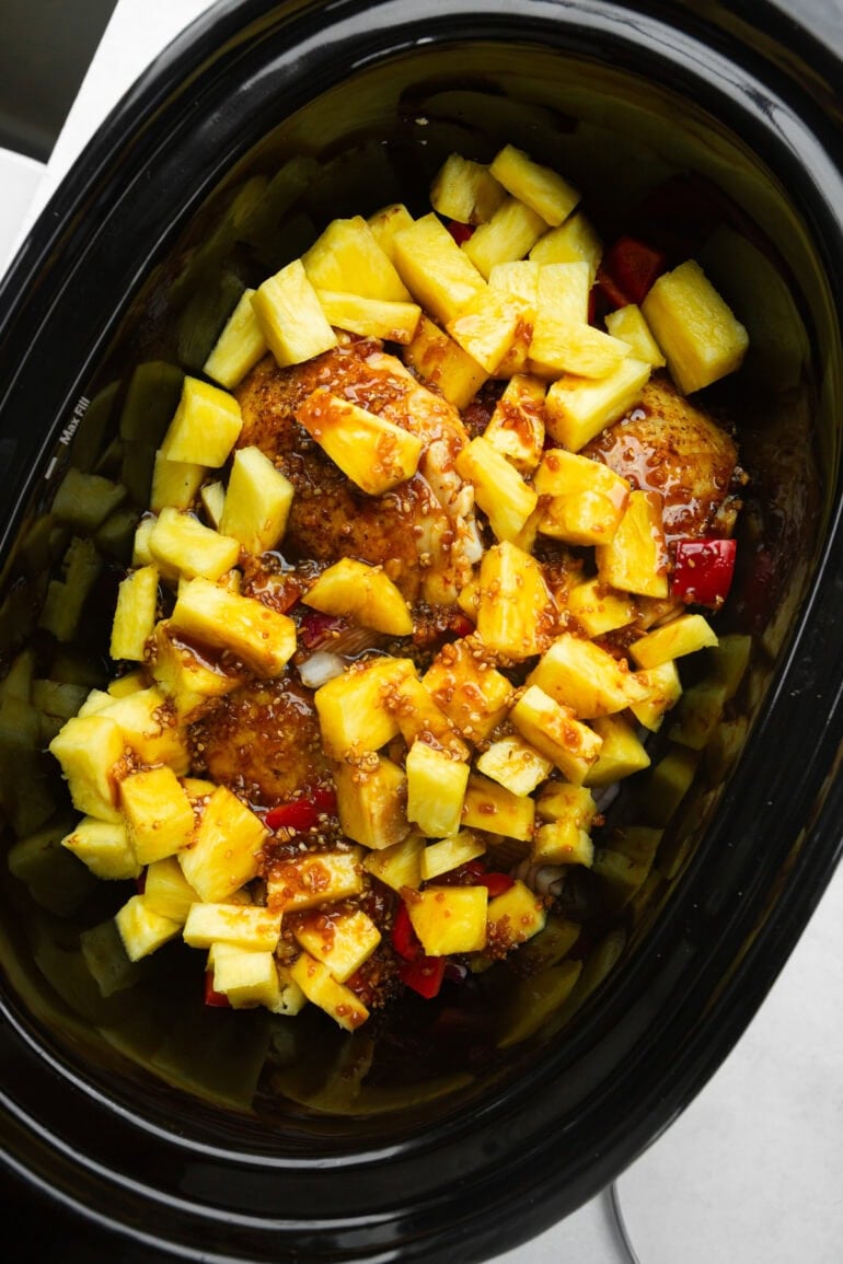 golden chicken thighs nestled in a cooking sauce topped with chunks of pineapple, red bell pepper and purple onion