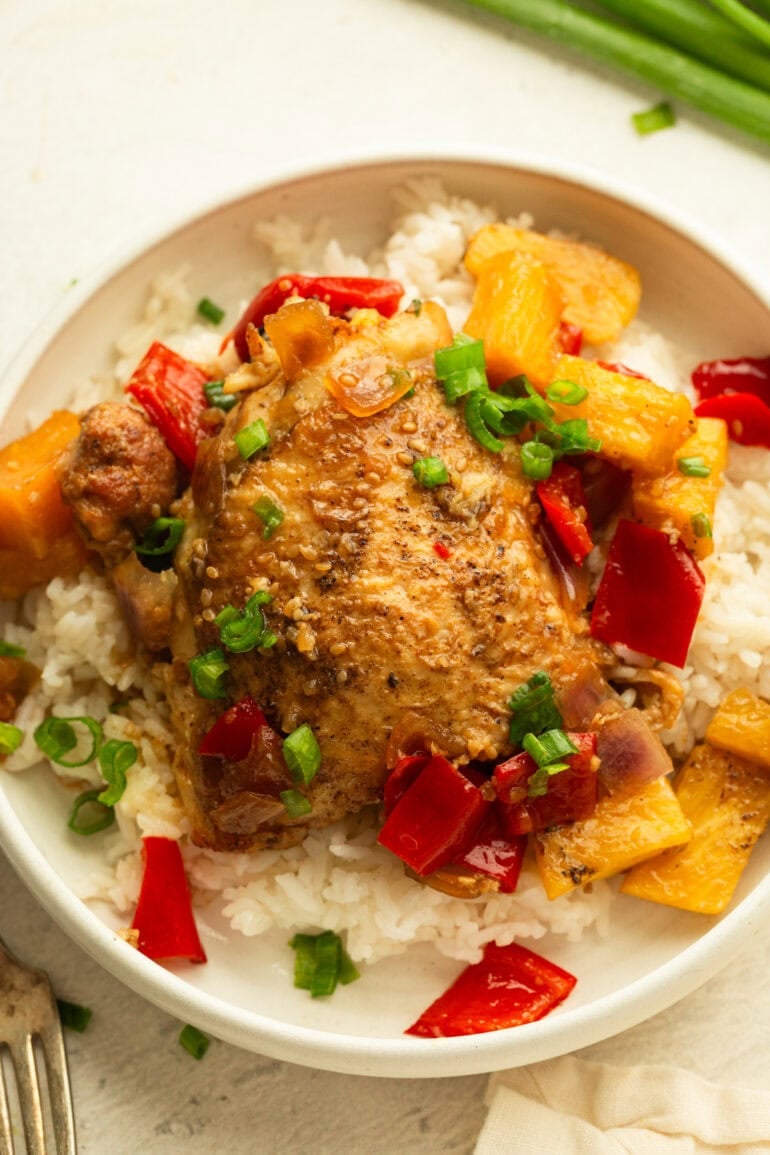 a dinner plate with a serving of white rice with bbq teriyaki chicken thigh and pineapple, bell peppers and onions over the top