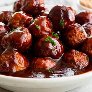a large serving bowl filled with saucy grape jelly meatballs