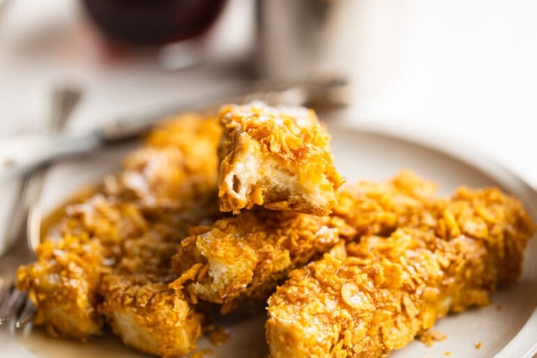 a pile of crunch french toast sticks with the one on top broken in half so that you can see the fluffy middle