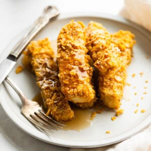 a stack of crunch french toast sticks sitting on a plate covered in syrup
