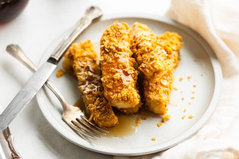 a stack of crunch french toast sticks sitting on a plate covered in syrup