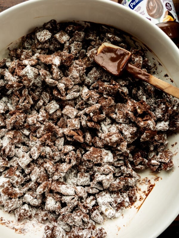 dark chocolate coated chex cereal being stirred in a white mixing bowl with a rubber spatula