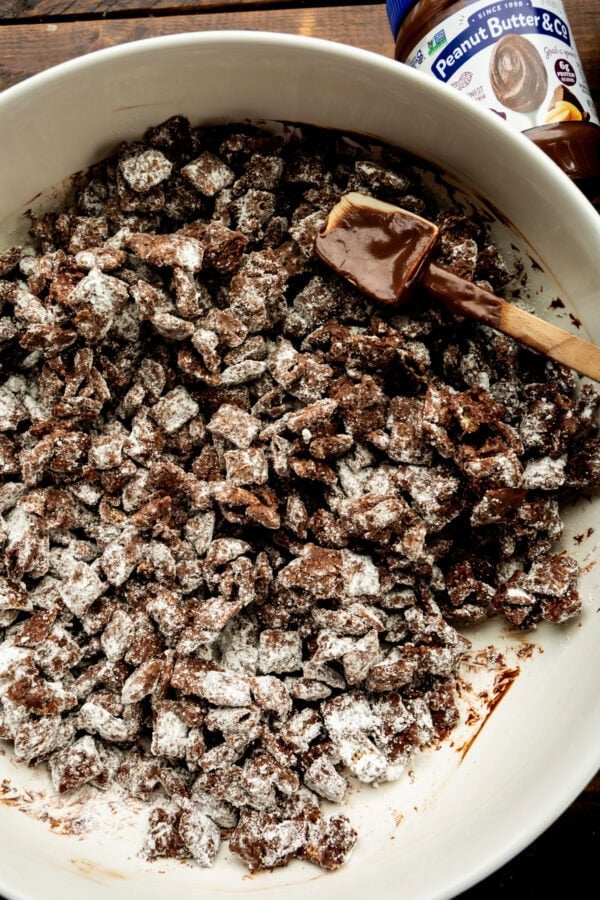 dark chocolate coated chex cereal being stirred in a white mixing bowl with a rubber spatula