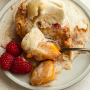 deep fried peach topped with a scoop of vanilla ice cream and fresh raspberries on the side