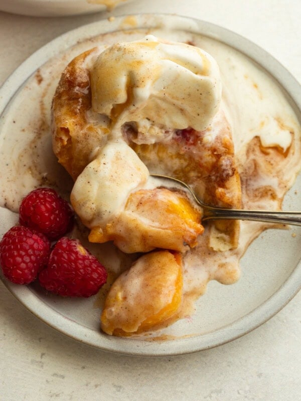 deep fried peach topped with a scoop of vanilla ice cream and fresh raspberries on the side