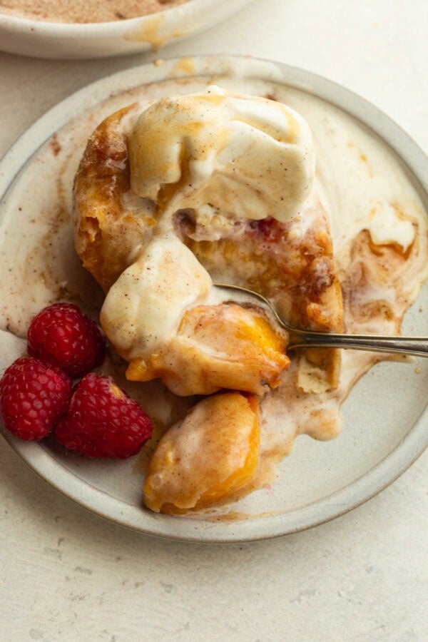 deep fried peach topped with a scoop of vanilla ice cream and fresh raspberries on the side