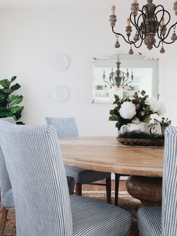 French Country Dining Room in white with natural wood, blue and white striped chairs, italian chandelier and round dining room table with pedestal leg ohsweetbasil.com