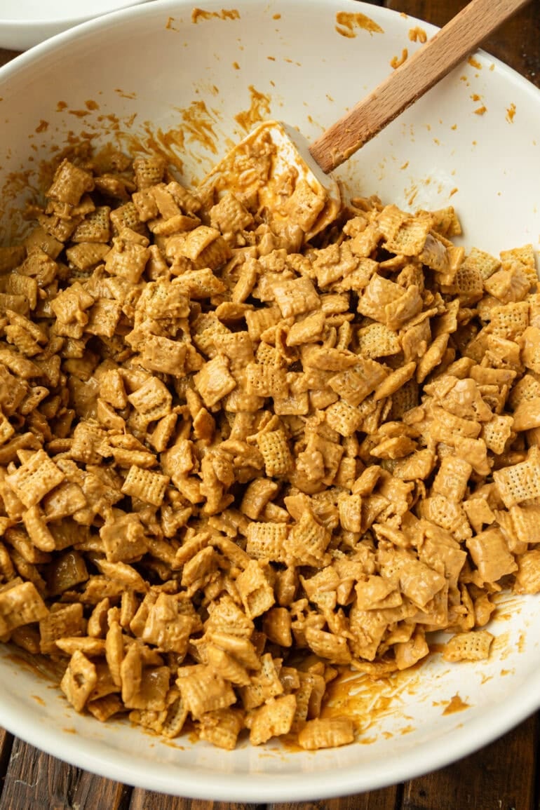 peanut butter muddy buddies being stirred in a large white mixing bowl