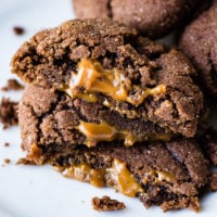 A photo of three dulce de leche stuffed chocolate cookies halved and stacked on top of each other with dulce de leche oozing out of the middle..