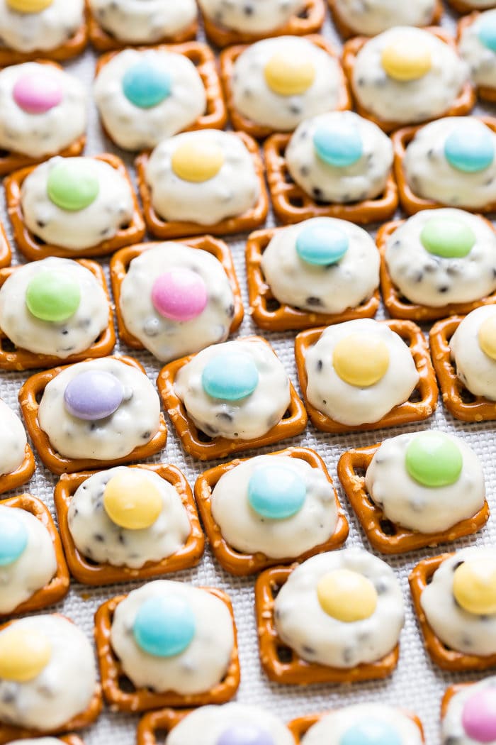 Hershey Kiss Pretzels evenly laid on a baking sheet. The pretzels have white chocolate melted treats with a little festive coated candy on top.