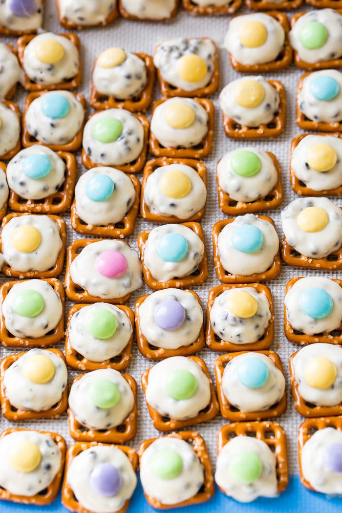 Many mini pretzels lined on a baking sheet with barely melted hershey's hugs topped with easter colored m&ms. Easter Pretzel Hugs with m&ms!