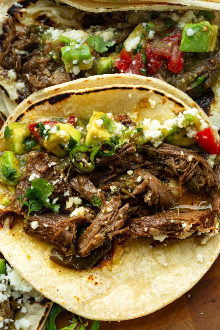 Overhead shot of shredded beef tacos loaded with juicy braised beef, roasted poblanos, fresh salsa, and crumbled queso fresco.