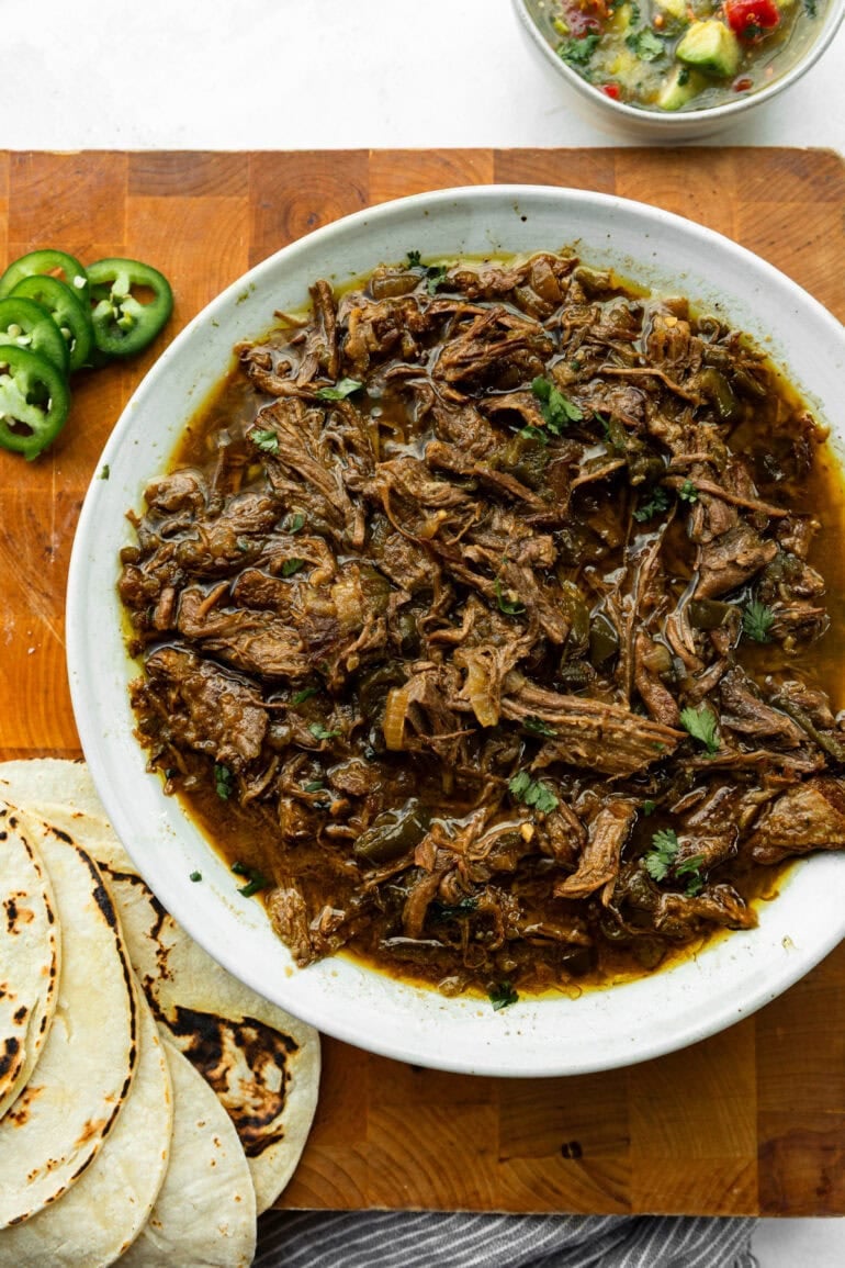 Close-up of juicy Mexican shredded meat alongside sliced jalapeños, and tortillas