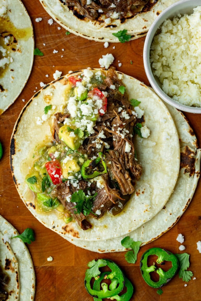 Overhead view of shredded beef tacos filled with flavorful meat, bright salsa, and melted queso fresco.