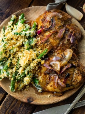 a photo of a wooden plate topped with two golden baked chicken thighs and a side of ranch green bean casserole.