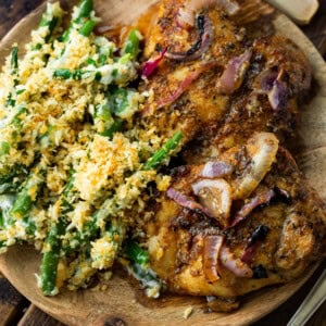 a photo of a wooden plate topped with two golden baked chicken thighs and a side of ranch green bean casserole.