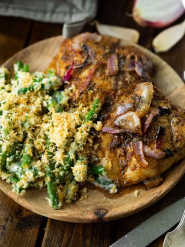 a photo of two baked chicken thighs sitting on a wooden plate next to a serving of ranch green bean casserole.