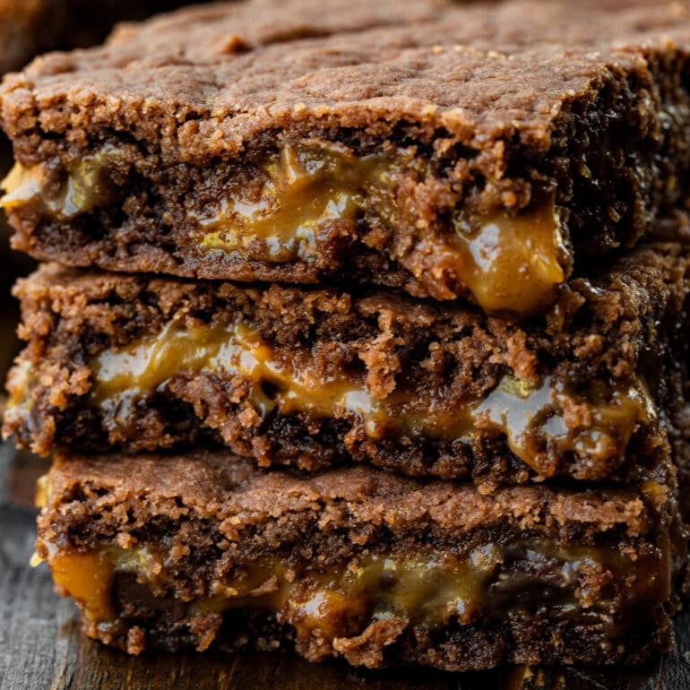 A stack of 3 layered brownies with a center layer of gooey caramel.