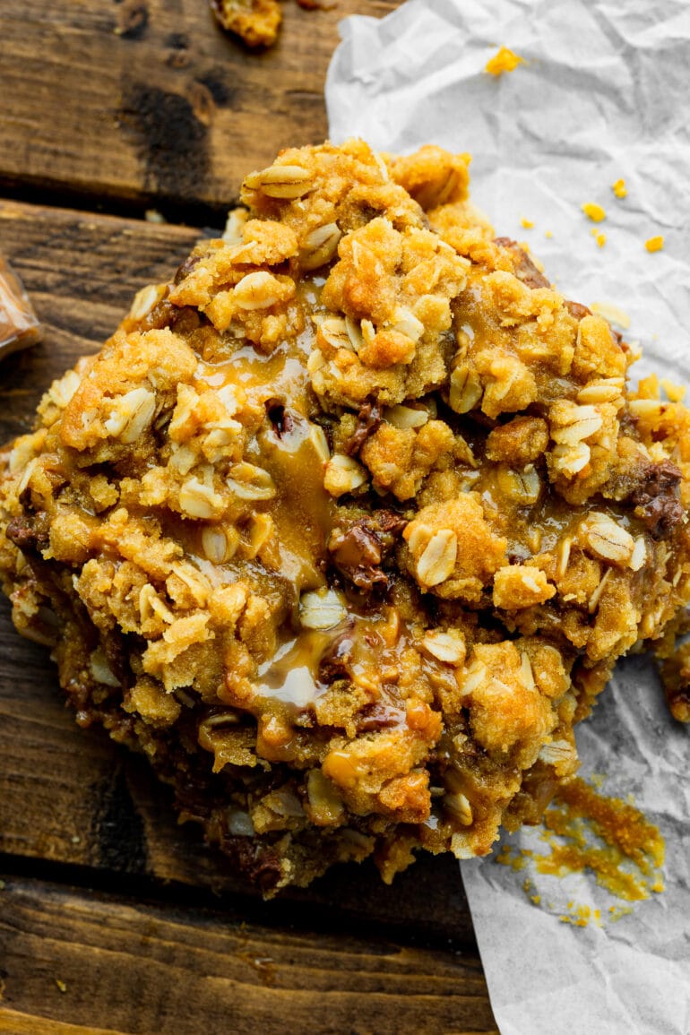 a square carmelita with a golden crispy oat topping with gooey caramel and melty chocolate oozing through it