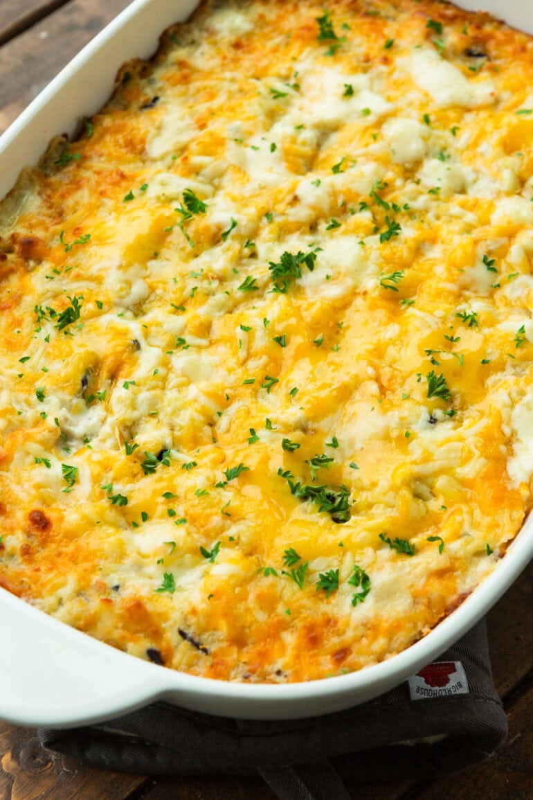 a photo of a chicken and rice casserole baked in a white casserole dish topped with melted cheese and chopped parsley