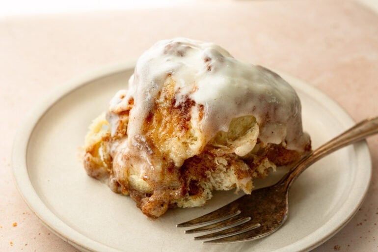 Fluffy piece of cinnamon bread being pulled from a round loaf of cinnamon pull apart bread with cream cheese frosting
