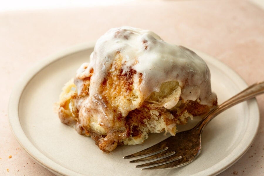 Fluffy piece of cinnamon bread being pulled from a round loaf of cinnamon pull apart bread with cream cheese frosting