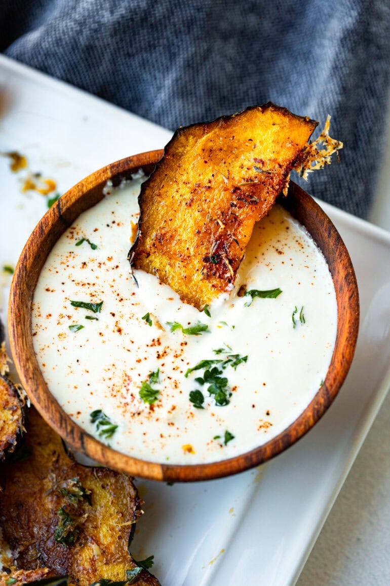 a photo of a piece of roasted acorn squash sitting partially in a small bowl of dip.