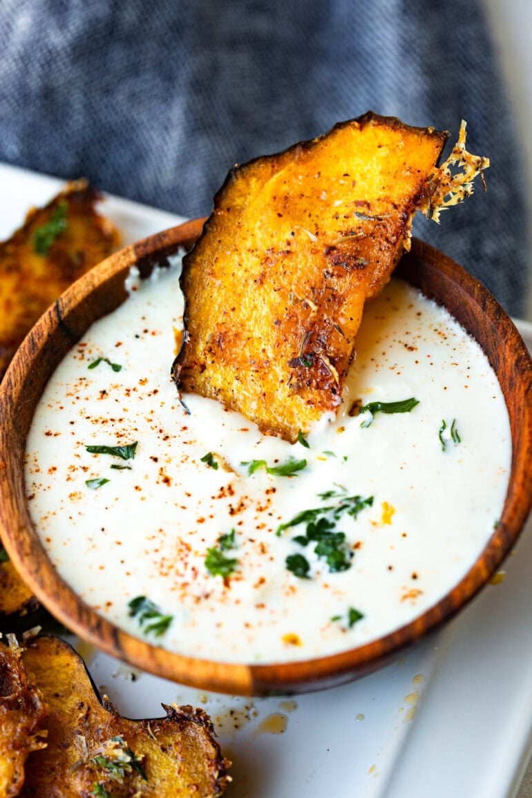 a photo of one slice of roasted acorn squash sitting halfway dipped in a small dish of dip