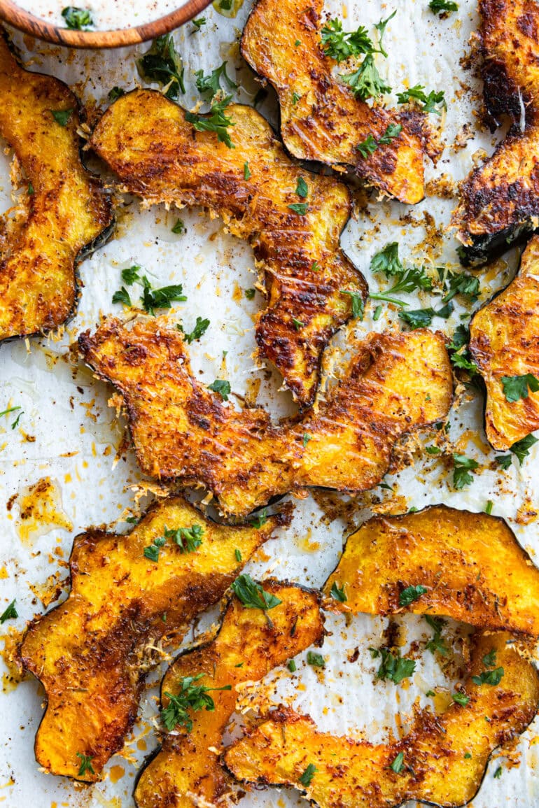 a photo of several slices of roasted acorn squash coated in crispy cheese and herbs
