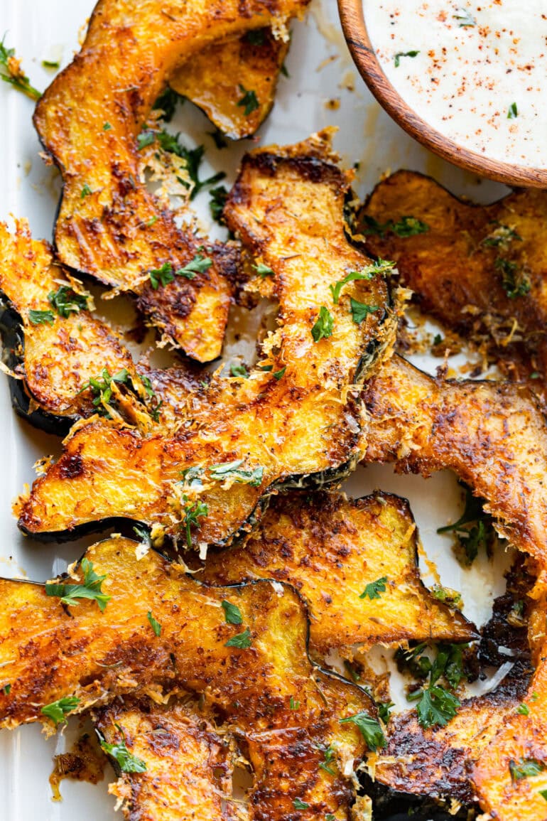 a photo of several slices of golden roasted acorn squash with crispy cheese and herbs