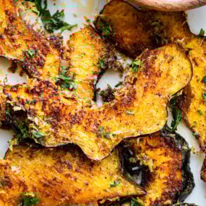 a photo of several slices of roasted acorn squash with fresh parsley sprinkled on top