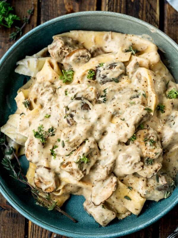 a photo of a bowl of creamy beef stroganoff mixed with egg noodles and mushrooms topped with fresh herbs