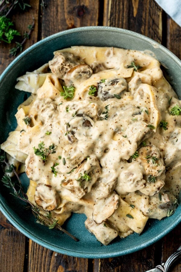 a photo of a bowl of creamy beef stroganoff mixed with egg noodles and mushrooms topped with fresh herbs
